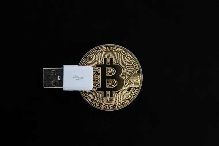 A gold Bitcoin coin next to a black USB hardware wallet on a dark surface