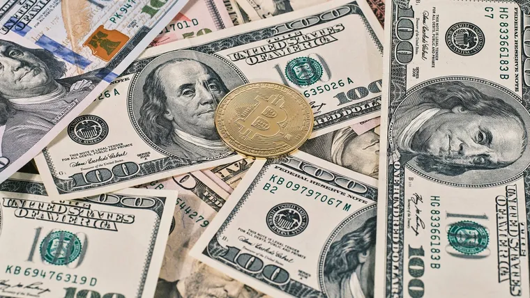 US$100 banknotes fanned out beside a gold Bitcoin coin, representing crypto sold for cash